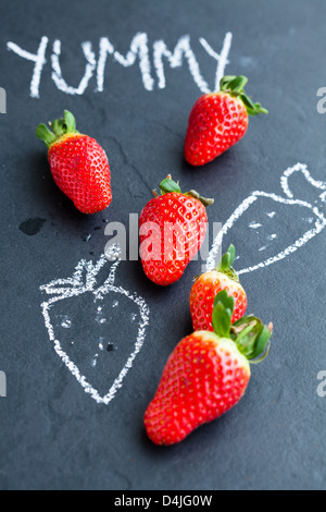 Ganze Erdbeeren und Kreidezeichnungen und lecker Wort auf dunklem Hintergrund Stockfoto