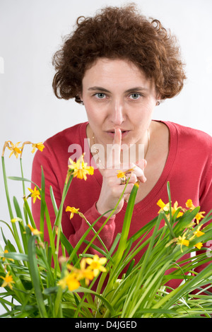 junge Frau mit lockigen Haaren und roten Pullover mit Finger vor den Lippen Stockfoto