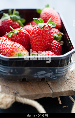 Ganze Erdbeeren in Plastikverpackung Tablett auf Holzuntergrund Stockfoto