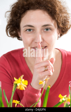 junge Frau mit lockigen Haaren und roten Pullover mit Finger vor den Lippen Stockfoto