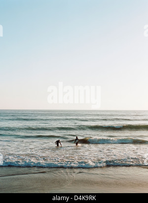 Surfer gehen in Wellen am Strand Stockfoto