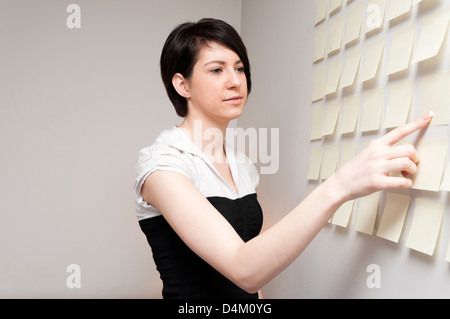 Junge Frau neben Wand des klebrigen Papier Notizen. Stockfoto