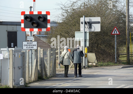 Alte im Alter von paar zu Fuß über eine automatische halbe Barriere Bahnübergang England uk Stockfoto