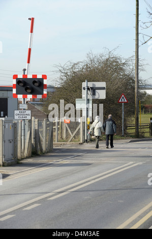 Alte im Alter von paar zu Fuß über eine automatische halbe Barriere Bahnübergang England uk Stockfoto