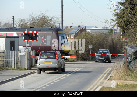 Ein d-Zug eine halbe Barriere Bahnübergang passieren, während Autos entweder Seite warten. Stockfoto