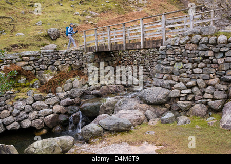 Ein Wanderer scheut Ghyll im Lake District eine Holzbrücke überqueren. Stockfoto