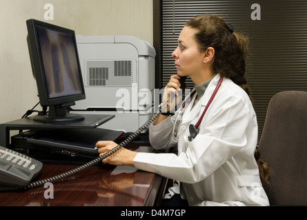 Junge Ärztin untersucht ein Röntgenbild der Brust und am Telefon sprechen Stockfoto