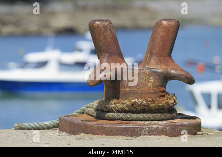 Ein heavy metal Stahl Liegeplatz Keil mit einem Boot Yacht schäbig gebunden Seil um auf einem Pier peir Hafen Hafen Kai gewickelt Stockfoto