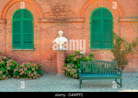 Holzbank stehen auf den Kies vor rotem Backsteinhaus mit geschlossenen grünen Fensterläden im Park von Racconigi in Piemont, Italien. Stockfoto