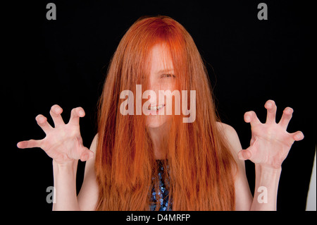 Mädchen mit langen roten Haaren bedeckte ihr Gesicht und das Tragen einer Brille vor einem schwarzen Hintergrund. Ihre Hände sind klauenartigen. Stockfoto