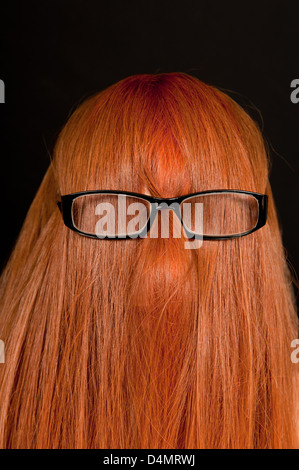 Mädchen mit langen roten Haaren bedeckte ihr Gesicht und das Tragen einer Brille vor einem schwarzen Hintergrund. Stockfoto