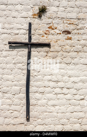 Ein rustikales Holzkreuz auf einer weißen Mauer Stockfoto