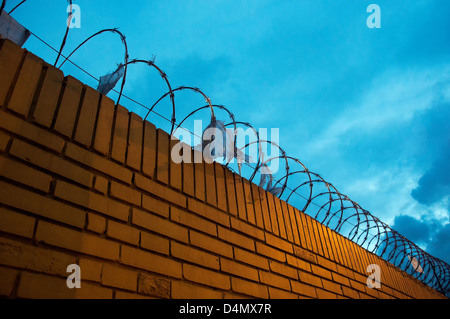 Einen gelben Backstein-Zaun mit Stacheldraht oben drauf Stockfoto