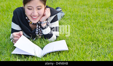 Asiatische Frau liest Notebook auf dem Rasen Stockfoto