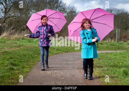 Zwei 8 jährige kaukasische Mädchen mit rosa Schirmen bergauf Stockfoto