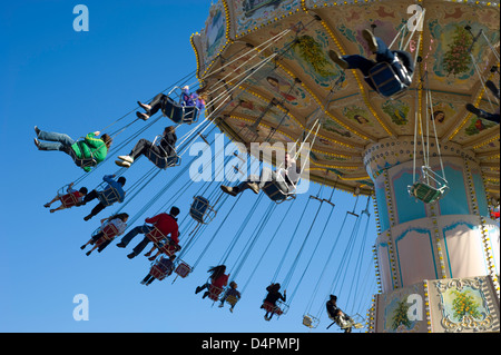 Eine gemischte Gruppe von Menschen in Höhe in auf einem Rummelplatz Stuhl fahren bei blauem Himmel im Hintergrund. Stockfoto