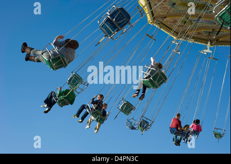 Eine gemischte Gruppe von Menschen in Höhe in auf einem Rummelplatz Stuhl fahren bei blauem Himmel im Hintergrund. Stockfoto