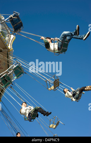 Eine gemischte Gruppe von Menschen in Höhe in auf einem Rummelplatz Stuhl fahren bei blauem Himmel im Hintergrund. Stockfoto