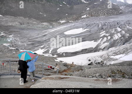 Ein paar steht unter einem Regenschirm, wie es den Rhone-Gletscher von einer Aussichtsplattform am Furkapass, Schweiz, 22. Juli 2009 Blick. Der Eingang zu einer Eisgrotte ist bedeckt mit Leinwand auf der rechten Seite im Vordergrund. Foto: Jochen Luebke Stockfoto