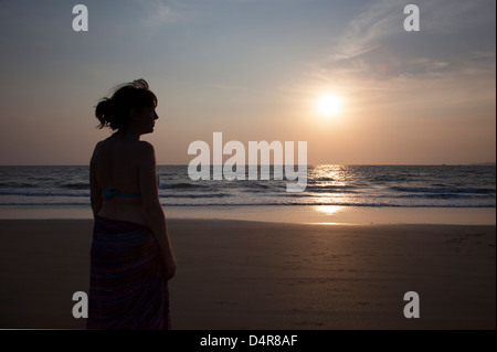 Setzen Sie auf Arossim Beach, Süd-Goa, Indien. Eine Frau blickt auf das Meer, wie die Sonne am Nachmittag. Stockfoto