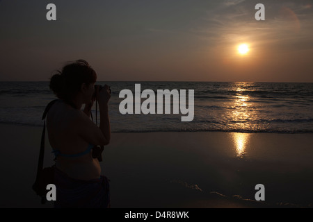 Eine weibliche Amateur-Fotografen schießen in die Sonne, wenn es über das Arabische Meer untergeht. Arossim Beach, Süd-Goa, Indien. Stockfoto