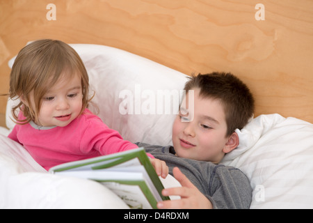 Kleine Schwester eine Frage zu seinem älteren Bruder über eine Seite im Buch bevor sie schlafen gehen. Stockfoto