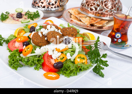 Falafel-Salat mit Fladenbrot und Hummus Platte, ergänzt mit Tee auf einer weißen Tischdecke. Stockfoto