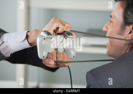 Geschäftsmann mit Videospiel-Controller-Kabel von Kollegen, beschnitten um Hals gebunden Stockfoto