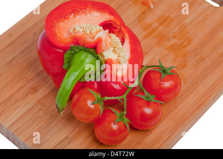 Paprika aufschneiden mit sichtbaren Samen auf einem Holzbrett mit Cherry-Tomaten Stockfoto