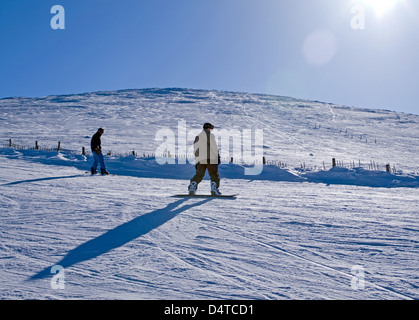 2 Snowboarder auf Piste, Cairngorm Mountain Bucht Marker auf Cairngorm Gipfel sichtbar hinter Stockfoto