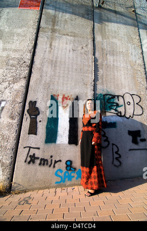 Eine stolze palästinensische Frau stehend durch die Barriere, die von der israelischen Regierung gebaut. Art und Graffiti schmücken diese Betonwand. Stockfoto