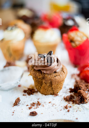 Ein Schokoladen-Kaffee-Muffin, umgeben von Krümel mit anderen Muffins im Hintergrund Stockfoto