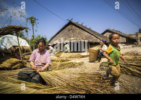 10. März 2013 - macht Samyekphoukhoun, Luang Prabang, Laos - eine Frau in einem Hmong Dorf am Highway 13 Stroh für eine Überdachung während ihres Sohnes in der Nähe spielt. Die Pflasterung der Autobahn 13 von Vientiane bis nahe der chinesischen Grenze hat den Weg des Lebens im ländlichen Laos verändert. Dorfbewohner in der Nähe von Luang Prabang verwendet zu haben, um unzuverlässige Boote nehmen, die drei Stunden hin-und Rückfahrt dauerte, bis aus den Häusern zum touristischen Zentrum von Luang Prabang, jetzt sie eine 40-minütige Rundfahrt nehmen Busfahrt. Nördlich von Luang Prabang wurde die Pflasterung der Autobahnanschluss eine Chance für China, Laos als eine Umladung Punkt zu verwenden. Chinesische merchand Stockfoto