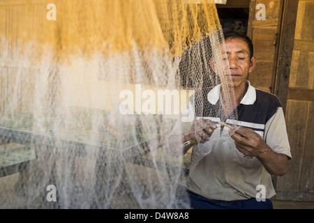 12. März 2013 - Ban Phon Xieng, Luang Prabang, Laos - arbeitet ein Fischer auf seine Netze auf der Veranda seines Hauses auf der Seite der Autobahn 13 in ländlichen Laos. Die Pflasterung der Autobahn 13 von Vientiane bis nahe der chinesischen Grenze hat den Weg des Lebens im ländlichen Laos verändert. Dorfbewohner in der Nähe von Luang Prabang verwendet zu haben, um unzuverlässige Boote nehmen, die drei Stunden hin-und Rückfahrt dauerte, bis aus den Häusern zum touristischen Zentrum von Luang Prabang, jetzt sie eine 40-minütige Rundfahrt nehmen Busfahrt. Nördlich von Luang Prabang wurde die Pflasterung der Autobahnanschluss eine Chance für China, Laos als eine Umladung Punkt zu verwenden. Chinesische Merchan- Stockfoto