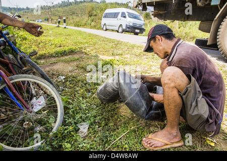 12. März 2013 - Ban Phon Xieng, Luang Prabang, Laos - behebt ein Mann eine Wohnung auf LKW entlang des Highway 13. Der LKW war Rohstoffe für Besen nach China schleppen. Die Pflasterung der Autobahn 13 von Vientiane bis nahe der chinesischen Grenze hat den Weg des Lebens im ländlichen Laos verändert. Dorfbewohner in der Nähe von Luang Prabang verwendet zu haben, um unzuverlässige Boote nehmen, die drei Stunden hin-und Rückfahrt dauerte, bis aus den Häusern zum touristischen Zentrum von Luang Prabang, jetzt sie eine 40-minütige Rundfahrt nehmen Busfahrt. Nördlich von Luang Prabang wurde ebnet der Autobahnanschluss eine Chance für China, Laos als Umladung Poi zu verwenden Stockfoto