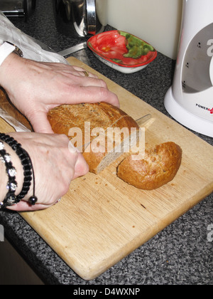 Frau, schneiden knuspriges Brot Laib auf Holzbrett Stockfoto