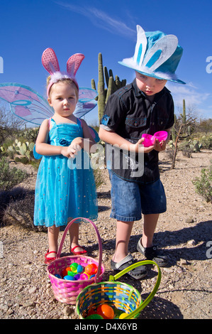 5 Jahre alter Bruder und 3 Jahre alte Schwester, die Spaß auf ein Osterei zu jagen in der Wüste tragen Hüte und Schmetterlingsflügel. Stockfoto