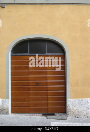 Gestreifte, zeitgenössische, hölzerne Garagentor auf einem hellen gelben Stuck-Haus auf einer schmalen Straße in Siena, Toskana, Italien Stockfoto