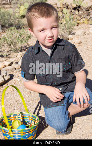 Ein fünf Jahre alter Junge hockt ohne sitzen direkt auf dem sandigen Wüstenboden. Stockfoto