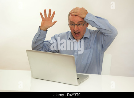 Überglücklich Mann hand auf Kopf mit Blick auf einem Laptop-Bildschirm, froh, dass er einen Preis gewonnen hat. Stockfoto