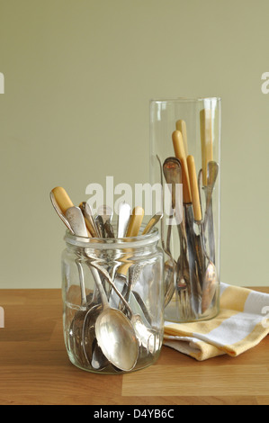 Vintage Besteck Silber mit Knochen verarbeitet in Gläsern auf Holztisch mit Vintage gelbe Geschirrtuch auf grün Stockfoto