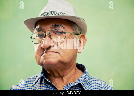 Menschen und Emotionen, Porträt von Ernst senior hispanic Mann mit Brille und Hut Blick in die Kamera vor grünem Hintergrund Stockfoto