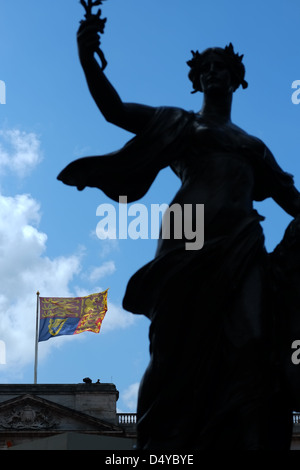 Eine Silhouette Statue steht außerhalb der Buckingham Palast mit der Royal Standard Fähnchen im Hintergrund. Stockfoto