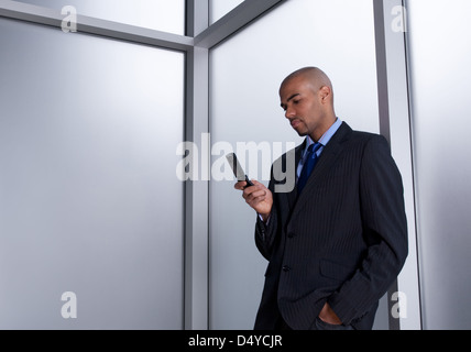 Geschäftsmann neben einem Büro-Fenster, das Senden einer Nachricht mit seinem Handy. Stockfoto