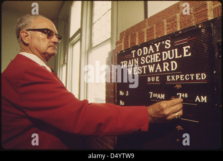 Amtrak-Bahnhof Agent in Dodge City, Kansas, platziert die voraussichtliche Ankunftszeit der Westbound Southwest Limited auf einem Zeitplan Bord als Teil seiner Aufgaben, Juni 1974 Stockfoto