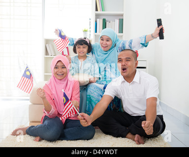 malaysische Familie feiert beim Fernsehen über ein Turnier, tragen einige Länderflaggen Stockfoto