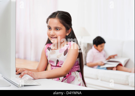 Mädchen mit Hilfe eines Computers mit ihrem Bruder ein Buch im Hintergrund Stockfoto