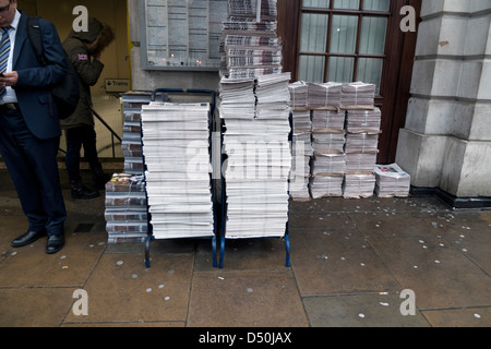 Gestapelte Zeitungen auf einem Zeitungskiosk außerhalb der U-Bahnstation und Geschäftsmann in Anzug lesen Papier Central London England UK KATHY DEWITT Stockfoto