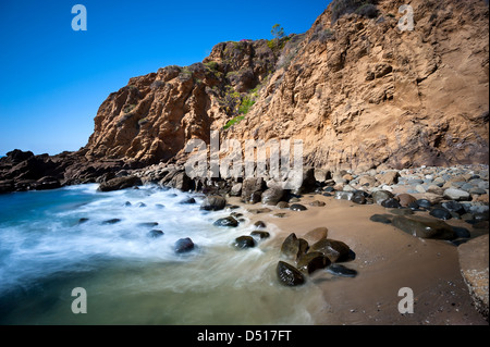 Eine einsame Abdeckung in Laguna Beach, Kalifornien zeigt das Meerwasser hetzen, um Ufer über glatten Felsbrocken. Stockfoto