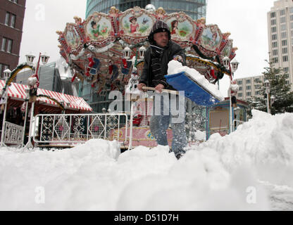 Ein Mann schaufelt Schnee vor einem Karussell am Potsdamer Platz in Berlin, Deutschland, 2. Dezember 2010. Die ersten Schneefälle in dieser Wintersaison haben die deutsche Hauptstadt erreicht. Foto: Kay Nietfeld Stockfoto